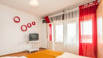 A bedroom with a bed, a television on a small table, and a window with red curtains.