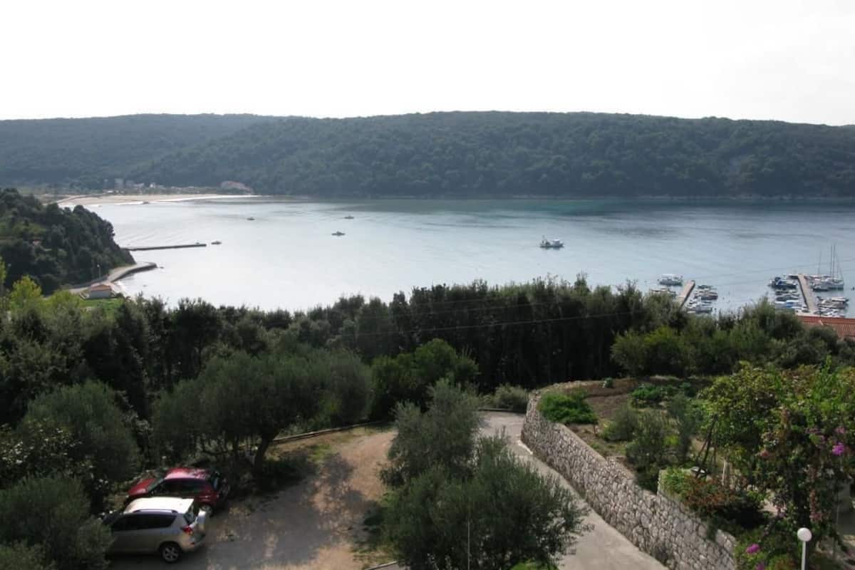 A coastal view with a marina, parked cars, and a stone wall.