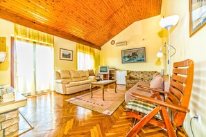 A spacious living room with a wooden ceiling, a sofa, a chair, a television, and a fireplace. - Apartment Belušić / Three Bedrooms A1 (Fazana)