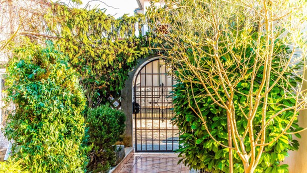 A garden pathway leading to a gated entrance, surrounded by lush greenery and a tiled floor. - Apartment Belušić / Three Bedrooms A1 (Fazana)