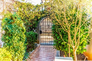 A garden pathway leading to a gated entrance, surrounded by lush greenery and a tiled floor. - Apartment Belušić / Three Bedrooms A1 (Fazana)
