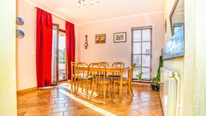 A dining area with a table and chairs, a red curtain, a radiator, and a window with blinds. - Apartment Belušić / Three Bedrooms A1 (Fazana)