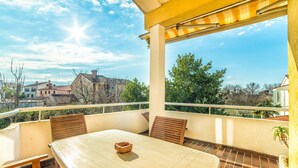 A balcony with a table and chairs, a potted plant, and a view of surrounding buildings. - Apartment Belušić / Three Bedrooms A1 (Fazana)