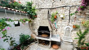 A stone-built outdoor kitchen area with a built-in grill, surrounded by potted plants and flowers. - Apartments Salčinović (Medulin)