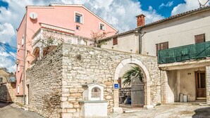 A stone building with a pink facade, a small arched entrance, and a satellite dish. - Apartments Salčinović (Medulin)