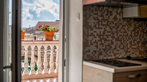 A kitchen with a tiled backsplash, a balcony with potted plants, and a view of the sky and buildings. - Apartments Salčinović (Medulin)