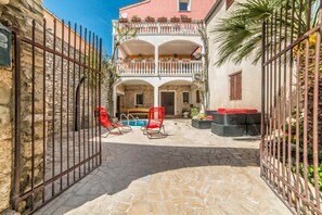Une cour avec un sol en pierre, une piscine, des chaises rouges et un balcon agrémenté de plantes.