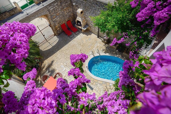 Une terrasse en pierre avec une piscine, des chaises longues rouges et des fleurs violettes.
