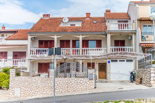 A multi-story building with a tiled roof, a stone wall, and a motorcycle parked in front.