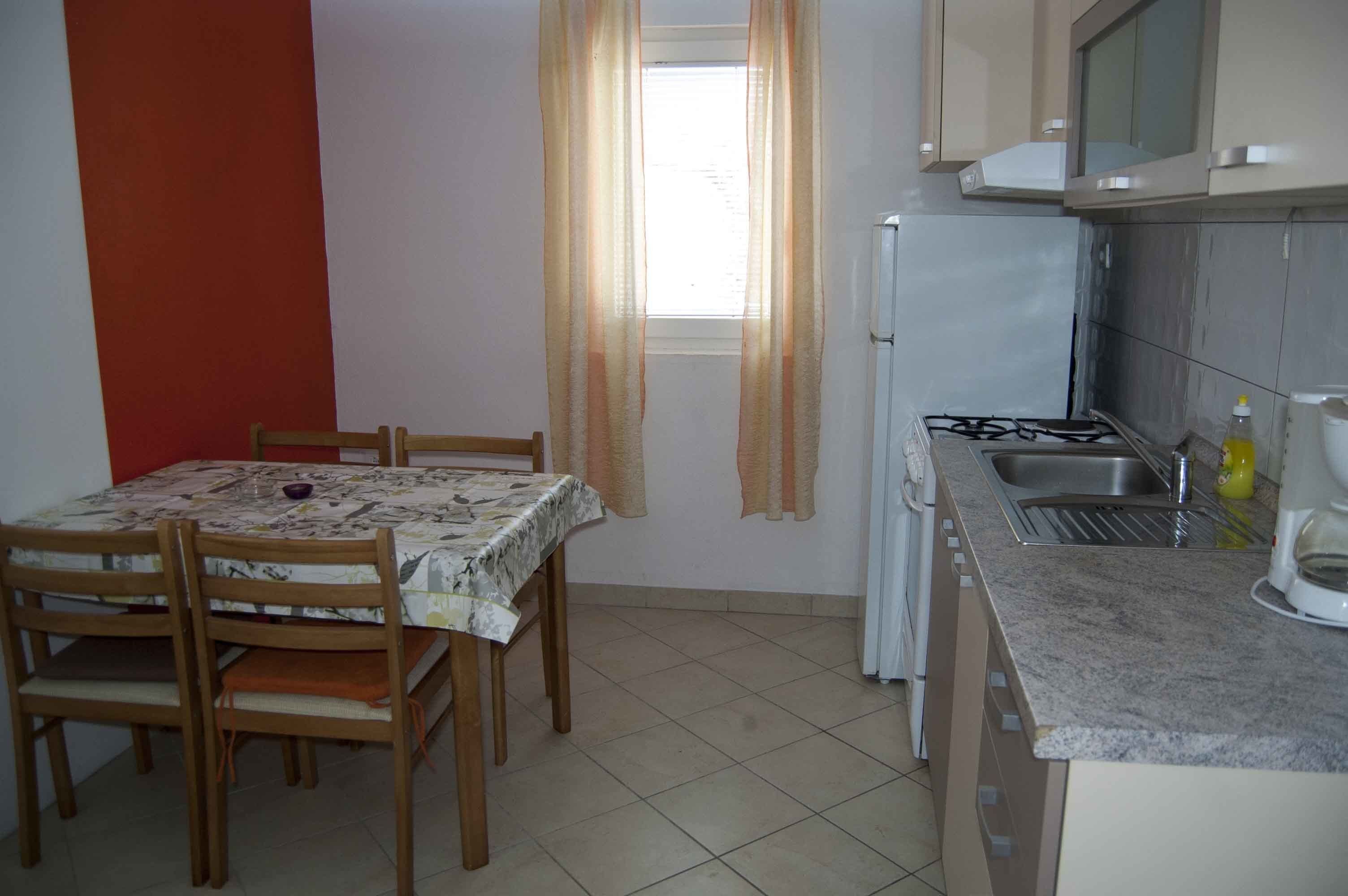 A compact kitchen with a dining table, chairs, a gas stove, a sink, and cabinets.