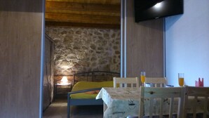 Una habitación acogedora con pared de piedra, una cama, una mesa con mantel y un televisor montado.