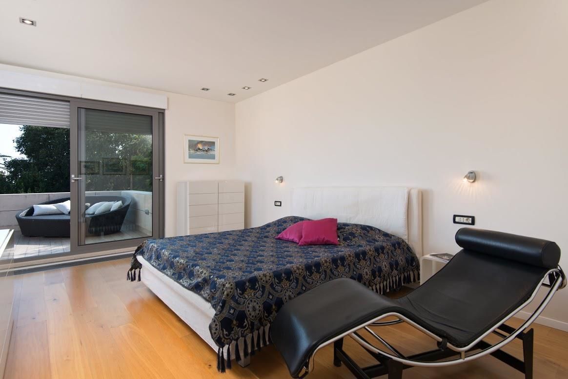 Quarto moderno com cama, chaise longue e porta de vidro deslizante que dá para uma área de estar externa.