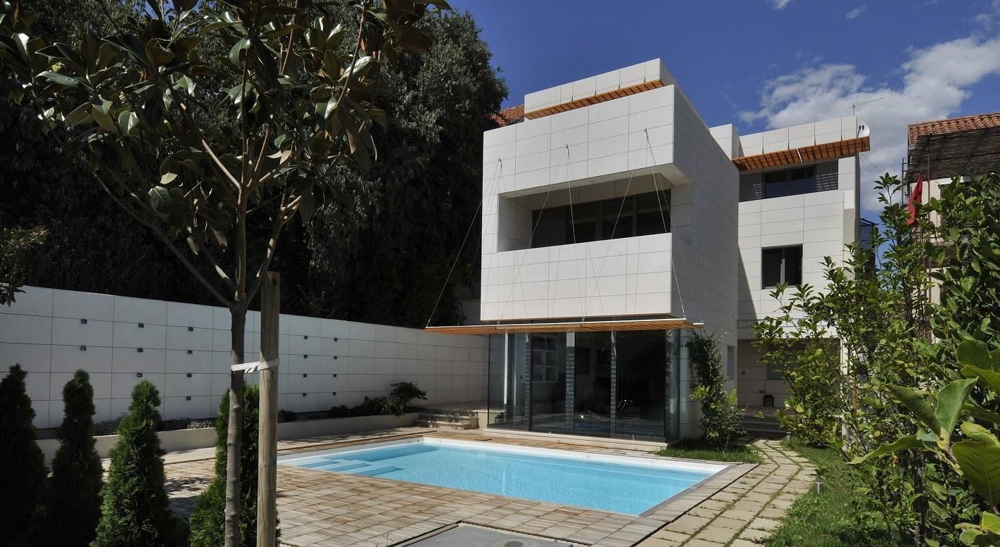Uma casa moderna de dois andares com piscina, cercada por vegetação e um muro branco.