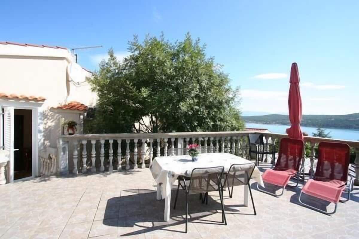 Une terrasse extérieure avec une table et des chaises, un parasol rouge et une vue sur la mer.