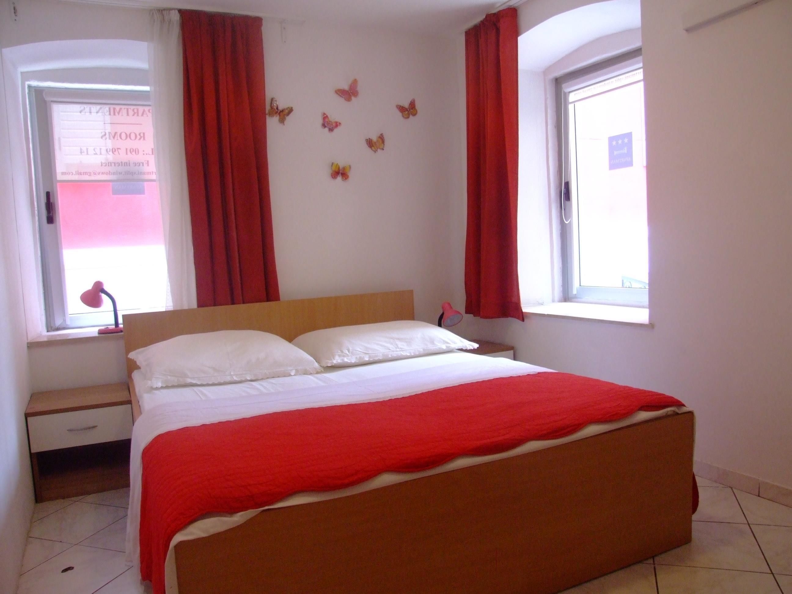 A bedroom with a bed, a window with curtains, a nightstand, and a wall with butterfly decorations.