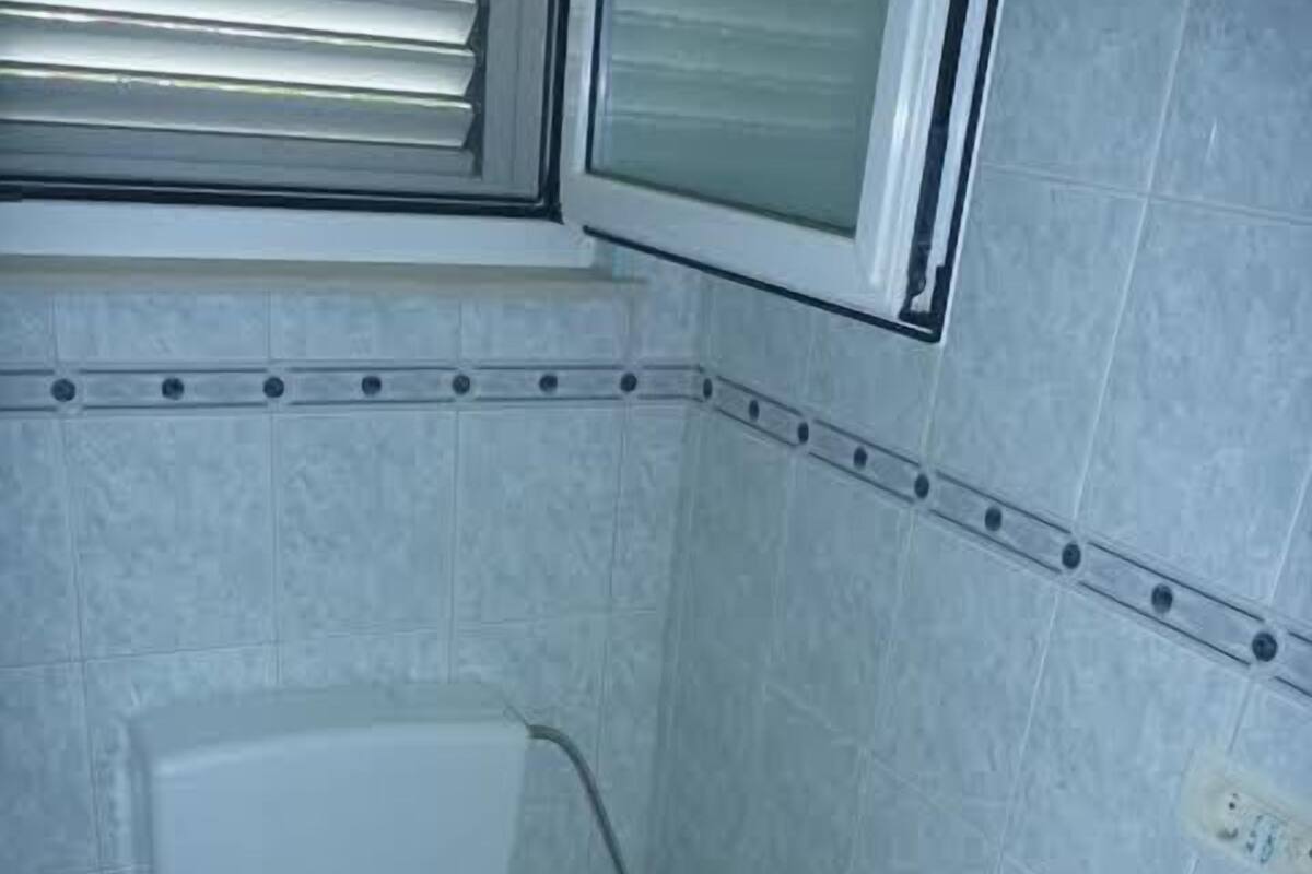 Un baño pequeño con azulejos, que incluye un inodoro, un bidé y una ventana sobre el inodoro.