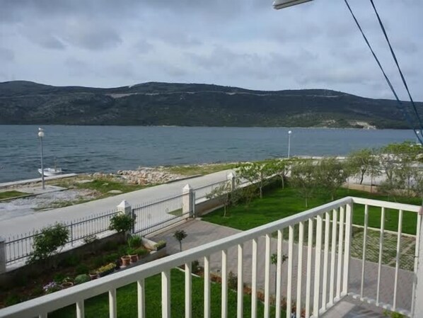 A balcony with a view of a lake, a pathway, and distant mountains.