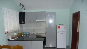A compact kitchen with a refrigerator, a sink, and a window with curtains.