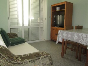 A bedroom with a bed, a green pillow, a wooden cabinet with a television, and a dining table with chairs.