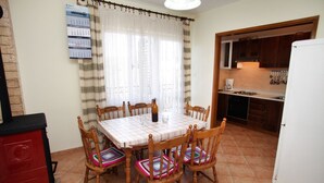 A dining area with a table set for four, wooden chairs with colorful cushions, a red cabinet, and a kitchen visible through an open door.