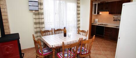 A dining area with a table set for four, wooden chairs with colorful cushions, a red cabinet, and a kitchen visible through an open door.