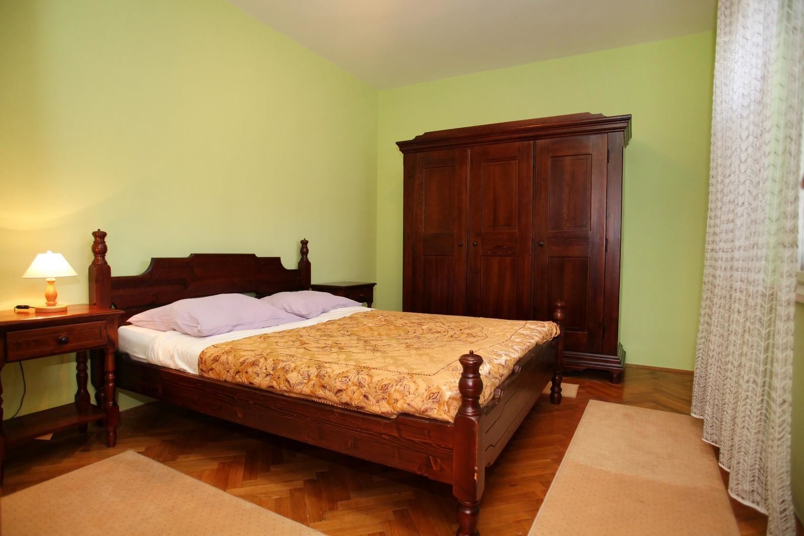 A bedroom with a wooden bed, a nightstand with a lamp, a wardrobe, and a patterned bedspread.