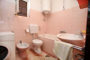 Et badeværelse med toilet, bidet, vaskemaskine og badekar.
