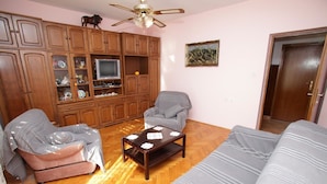 A living room with a sofa, two armchairs, a coffee table, wooden cabinets, a television, and a ceiling fan.