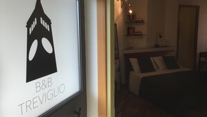A hotel room with a bed, a nightstand, and a shelf with books and a lamp. - B&B Treviglio (Treviglio)