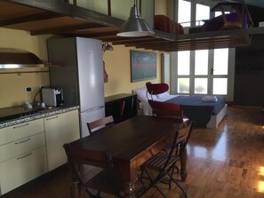 A kitchen with a refrigerator, stove, and coffee maker. There is a dining table with chairs and a window with a view of the outside. - B&B Treviglio (Treviglio)