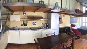 A compact kitchen with a dining area, a red chair, and a bed in the adjacent room. - B&B Treviglio (Treviglio)