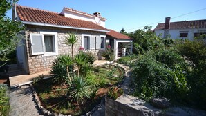 Een stenen huis met een pannendak, een tuin met verschillende planten, en een stenen muur.