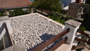 Een terras op het dak met een grindvloer, omgeven door een witte muur en houten hekwerk.