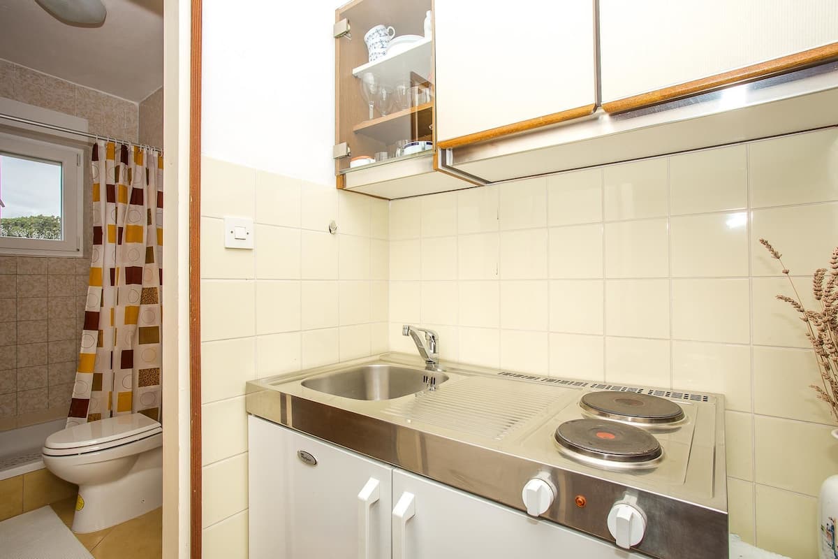 A compact kitchen with a built-in sink, stove, and a small cabinet above the sink.