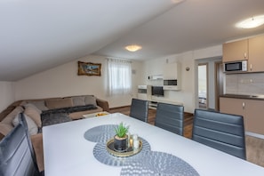 Un salon moderne avec une table à manger blanche, des chaises noires et un canapé beige.