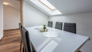 A modern dining area with a white table, black chairs, and a skylight above. - Apartments Mirela (Crikvenica)