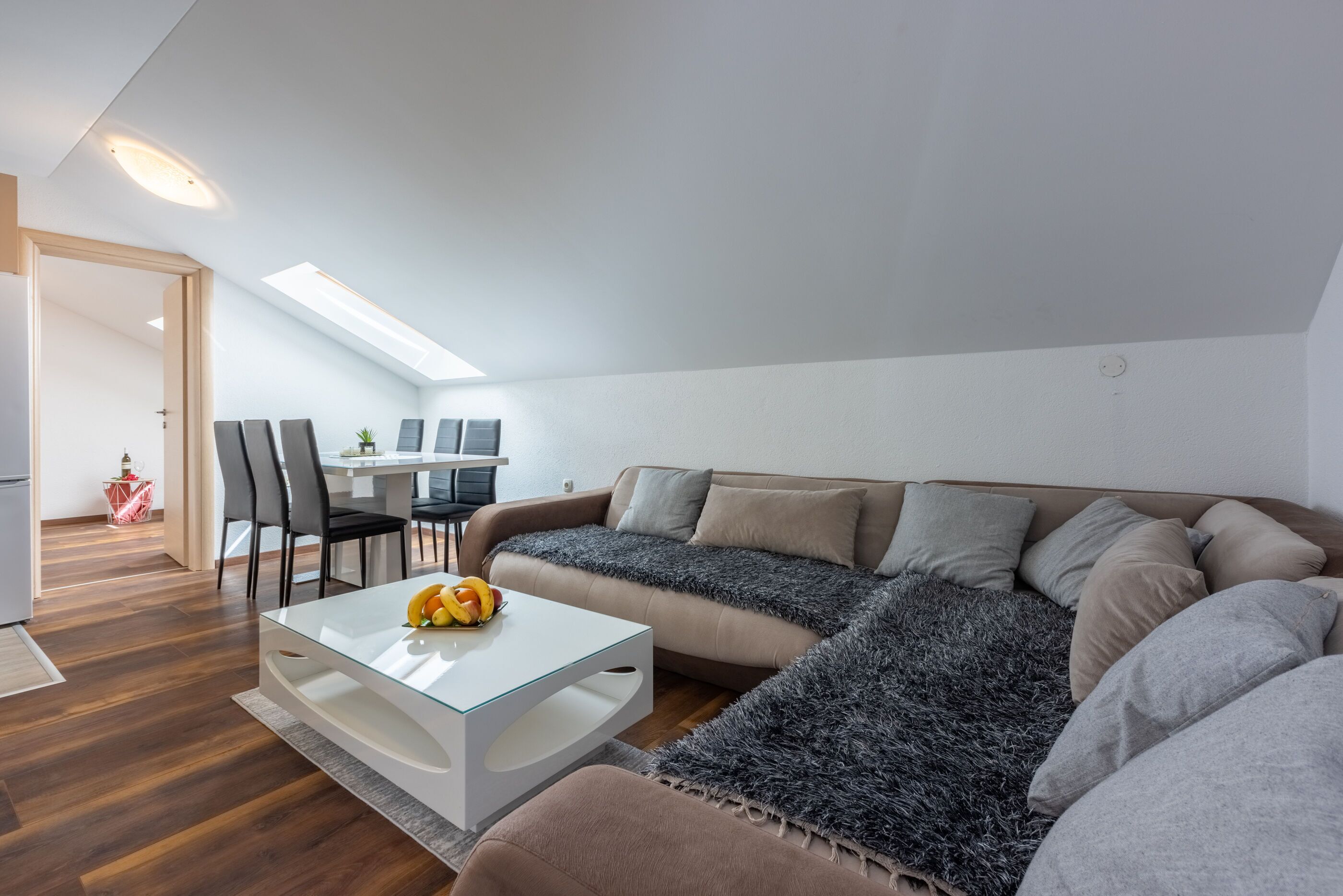A modern living room with a glass coffee table, a sofa, and a dining area with chairs and a table.