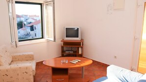 Una habitación pequeña y luminosa con un sofá, una mesa de centro, un televisor sobre un mueble y una ventana con vistas a edificios.