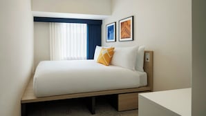 A neatly made bed with a wooden frame, a bedside table, and two framed pictures on the wall.
