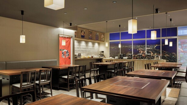A restaurant with wooden tables and chairs, a counter with a menu, and a view of the city at night.