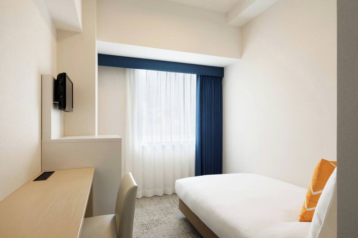 Ein Hotelzimmer mit Bett, Schreibtisch und einem Vorhangfenster.