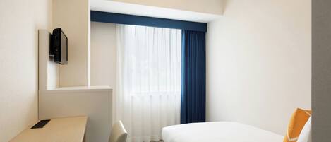 A hotel room with a bed, a desk, and a window with curtains.