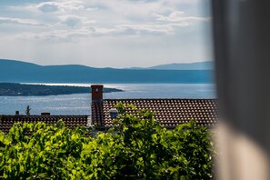 Une vue d’une terrasse avec un toit recouvert de tuiles, une cheminée et une végétation luxuriante au premier plan.