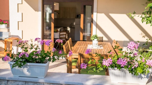 An outdoor dining area with wooden tables and chairs, surrounded by potted plants with purple flowers. - Holiday House Ivana (Malinska-Dubasnica)