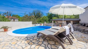 A swimming pool with lounge chairs and an umbrella, surrounded by stone tiles and greenery. - Holiday House Ivana (Malinska-Dubasnica)