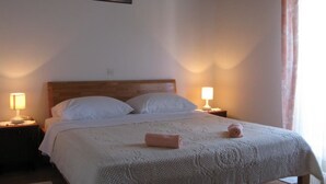 A neatly made bed with a white bedspread and two pillows, two bedside lamps, and a painting on the wall. - Apartments Mahić (Rab)