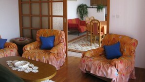A living room with two orange armchairs, a wooden coffee table, and a sliding glass door leading to a dining area. - Apartments Mahić (Rab)