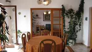 A dining room with a round table, chairs, and a patterned rug. There are potted plants and a television in the background. - Apartments Mahić (Rab)