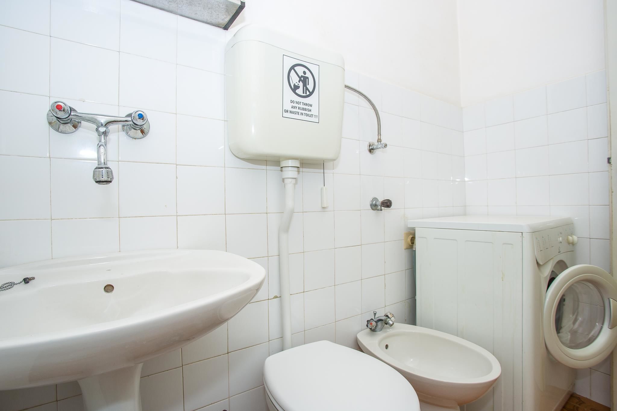A bathroom with a sink, toilet, bidet, and a washing machine.