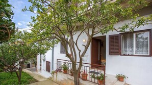 A white building with a balcony, potted plants, and a tree in front. - Apartments Pinsa (Okrug)